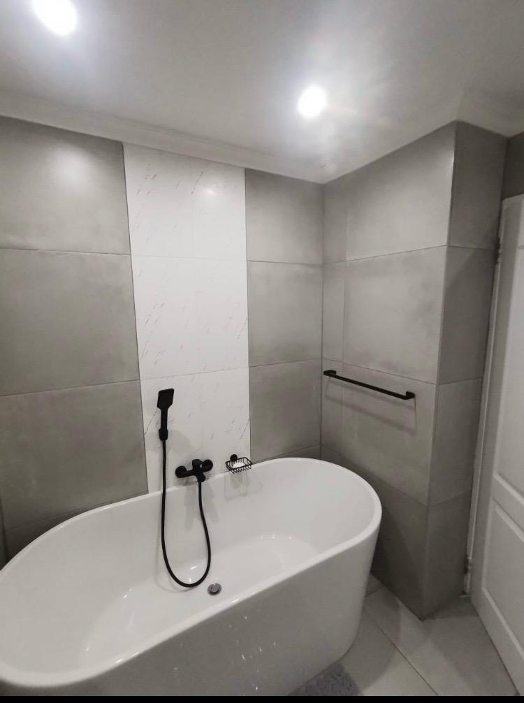 Modern bathtub installation with grey wall tiles and black fittings