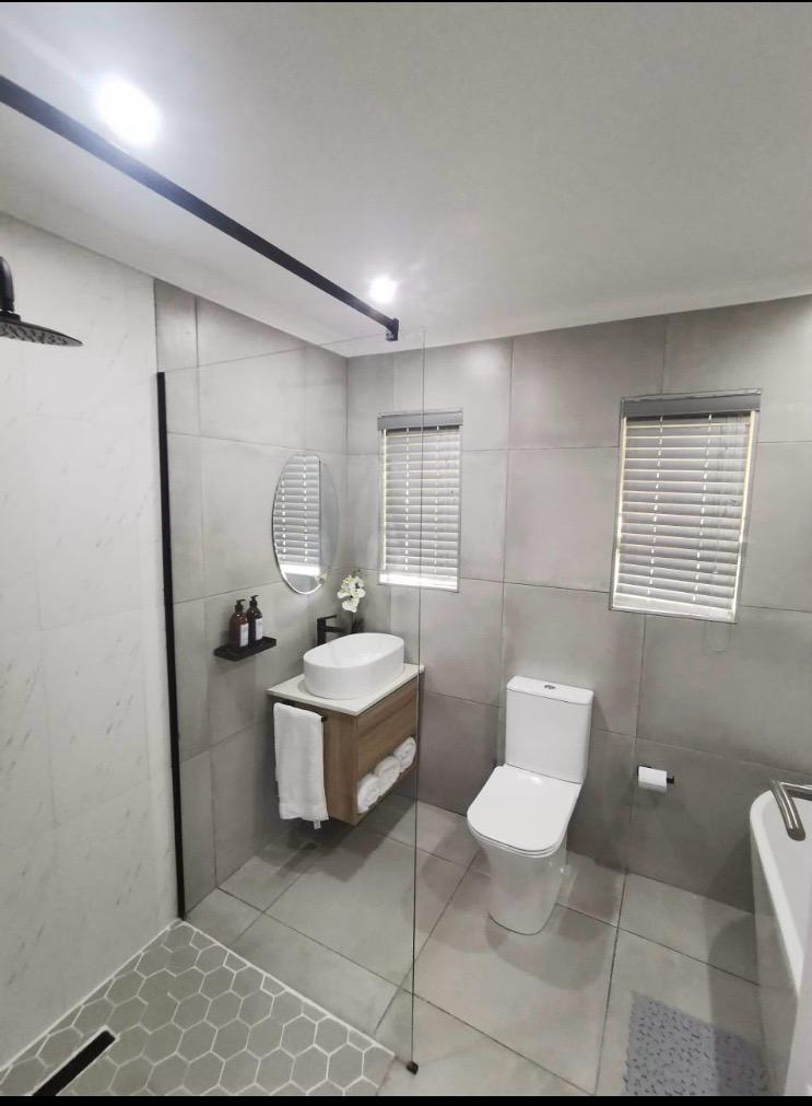 Finished bathroom with shower, vanity, toilet and grey wall tiles